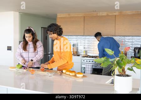 Diversi amici tagliano e assemblano panini sull'isola bianca in una cucina moderna con panini Foto Stock