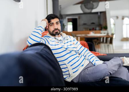 Uomo indiano sdraiato su un divano in velluto blu scuro, che guarda la macchina fotografica in uno spazio abitativo open space Foto Stock