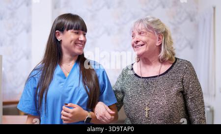 Infermiera che assiste una donna anziana che cammina, sorride in una casa di cura Foto Stock