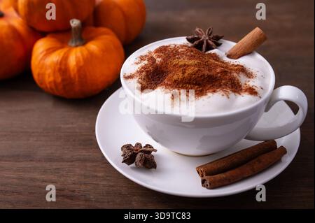 La bevanda di zucca con succo di zucca latte e panna montata si trova in una tazza bianca. Le zucche e i bastoncini di cannella sono circondati da un'atmosfera autunnale Foto Stock