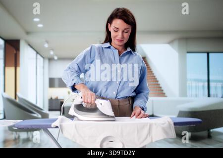 Donna che crea stampe di T-shirt personalizzate con Iron Appliance a casa Foto Stock