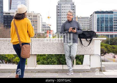 Diverse coppie anziane in piedi sul balcone sul tetto con ringhiere e borsa da palestra mentre tengono in mano gli smartphone Foto Stock