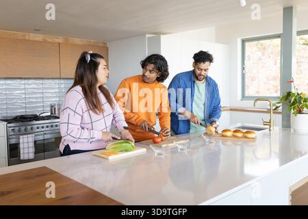 Diversi amici tagliano gli ingredienti con tavole di legno vicino alle ciotole di vetro sull'isola bianca della cucina Foto Stock