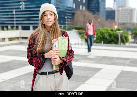 Adolescente in piedi in piazza con una cartella verde e un luminoso notebook con zaino Foto Stock