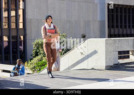 Diverse studentesse che salgono i gradini tenendo un taccuino e una cartella, leggendo un libro di testo sulla terrazza Foto Stock