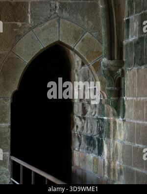 Arco gotico in pietra all'interno della storica Abbazia di Mont Saint-Michel. Dettagli architettonici medievali caratterizzati da un arco a punta e pareti in pietra intemprata. Foto Stock