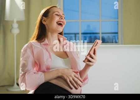 Maternità gravidanza. Donna incinta con smartphone che scrive scorrendo a casa. Donna con cellulare che si diverte a navigare su Internet utilizzando le app di social media. Applicazione mobile per donne in gravidanza || modello rilasciato Foto Stock