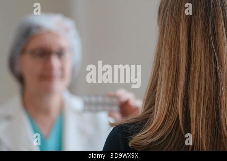 Primo piano da dietro mostra un'infermiera in uniforme bianca che consegna la medicina a una paziente. Enfatizza le cure mediche, il supporto sanitario e la fiducia dei pazienti nelle cure ospedaliere. || modello rilasciato Foto Stock