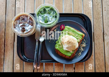 Set di pane tostato a fette con gelato alla vaniglia, crema pasticcera al vapore con caffè freddo, latte matcha freddo servito in vassoio nero su un tavolo di legno Foto Stock