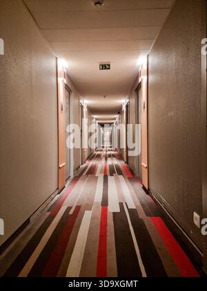 Lungo corridoio vuoto dell'hotel con tappeto a righe, con segnale di uscita di emergenza Foto Stock