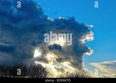 Una spettacolare nuvola di tempesta che passa contro un cielo azzurro limpido con il sole che retroillumina la formazione Foto Stock