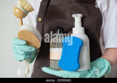 Donna che indossa guanti che contengono una varietà di prodotti per la pulizia e utensili ecologici per le faccende domestiche Foto Stock