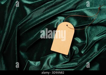 Etichetta marrone vuota appoggiata su un lussuoso panno di velluto verde con eleganti tendaggi Foto Stock