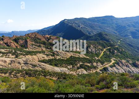 La tortuosa strada sterrata si snoda attraverso le aspre montagne della California meridionale, rivelando impressionanti formazioni rocciose e lussureggianti cappelle verdi sotto un blu chiaro Foto Stock
