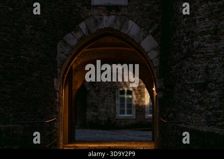 Storico arco in pietra illuminato dalla calda luce serale nella città vecchia di Boulogne-sur-Mer, Francia. Passaggio medievale con muri in pietra. Foto Stock