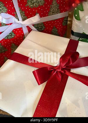 Sfondo natalizio con un regalo bianco con fiocco rosso pronto per regali e altri regali. Tema rosso, bianco e verde. Foto Stock