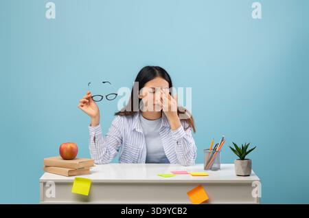Lo studente lotta con Focus mentre studia a una scrivania piena di note e una mela in una stanza azzurra Foto Stock