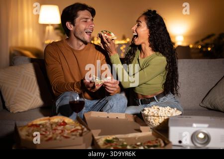I coniugi condividono piacevoli spuntini di pizza mentre si godono la serata del cinema a casa Foto Stock