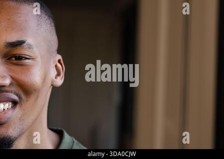 Uomo sorridente in piedi nel corridoio beige, indossa una camicia verde e brilla sotto una luce calda Foto Stock