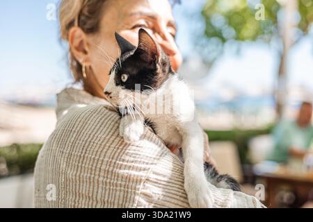 una donna di mezza età tiene in braccio un piccolo gatto bianco e nero Foto Stock
