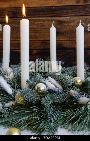 Due alte candele bianche bruciano delicatamente sopra una festosa corona sempreverde decorata con ornamenti dorati e rami smerigliati. Foto Stock