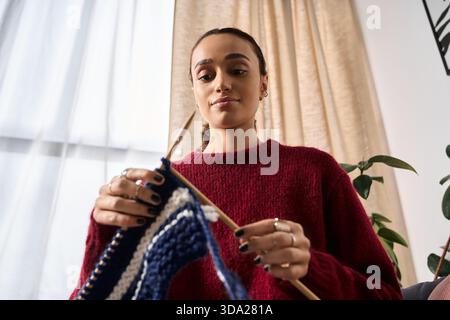 Una giovane donna afroamericana ama lavorare a maglia nel suo moderno appartamento durante l'inverno. Foto Stock