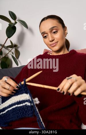 Una giovane donna ama trascorrere un pomeriggio tranquillo a maglia nel suo elegante appartamento. Foto Stock