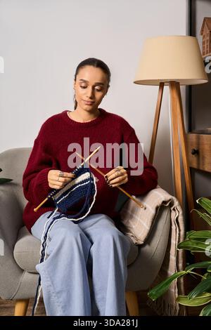 Una giovane donna afroamericana ama lavorare a maglia nella sua elegante casa, abbracciando la creatività. Foto Stock