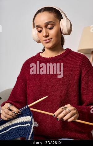 Una giovane donna ama lavorare a maglia indossando un maglione marrone nel suo elegante spazio abitativo. Foto Stock