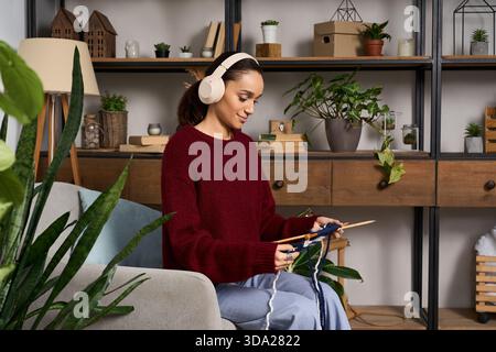 Una giovane donna ama lavorare a maglia mentre si rilassa nel suo elegante appartamento, indossando un comodo maglione. Foto Stock