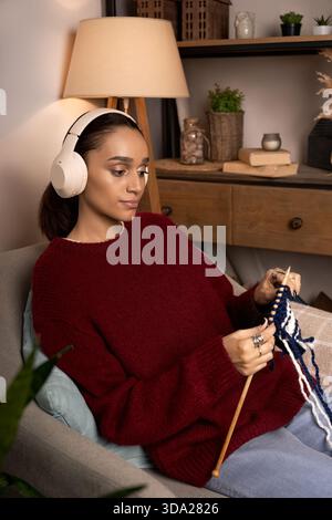 Una giovane donna ama lavorare a maglia mentre si rilassa a casa con il suo elegante maglione invernale. Foto Stock