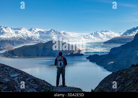 Uomo affacciato sul ghiacciaio Grigio e sul Lago Grigio circondato da montagne innevate del massiccio del Paine lungo il percorso escursionistico W-Trek a Torres del Paine nati Foto Stock