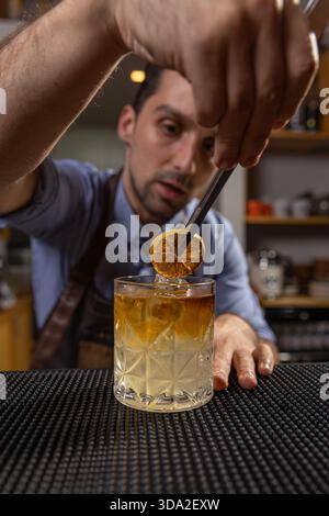 Barman che guarnisce con cura un cocktail con arancia secca in un bar Foto Stock