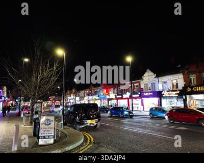 Salford, Regno Unito - 8 novembre 2025: Vivace vista notturna di Salford, Regno Unito, con negozi al neon, auto in movimento e pedoni lungo una strada vivace. Foto Stock