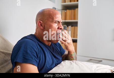 Sbadiglio uomo che si rilassa sul divano a casa con Libreria sullo sfondo Foto Stock