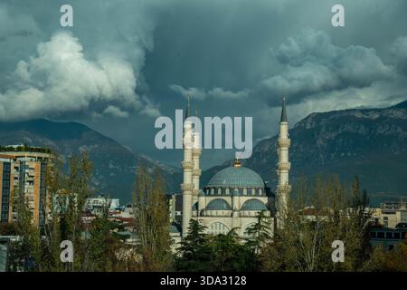 La grande moschea di Namazgah e minareti a Tirana, Albania, è ambientata contro montagne scure e spettacolari e un cielo coperto. Foto Stock