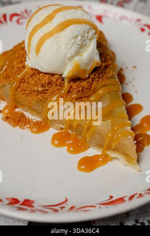Una porzione di torta di mele con gelato alla vaniglia su un piatto. Strudel di mele caldo con una pallina di gelato sullo sfondo di mele verdi e un tavolo Foto Stock