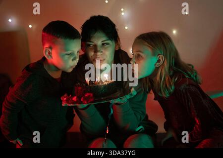 La famiglia fa saltare le candele di compleanno sulla torta al cioccolato Foto Stock