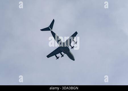 Quattro motori turboelica sponde aerei attraverso il cielo in una spettacolare vista dal basso. La silhouette scura e le eliche rotanti attraversano nuvole alte. Foto Stock