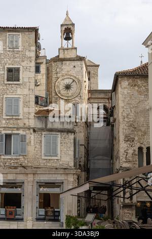 Un paesaggio urbano europeo illuminato dal sole caratterizzato da edifici in pietra intemprata, un orologio e un campanile di primo piano, e terrazze sul tetto con ombrelloni, che evocano il vecchio stile Foto Stock
