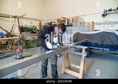 Uomo che si occupa di progetti di lavorazione dei metalli, indossando occhiali e guanti di sicurezza in un'officina industriale Foto Stock