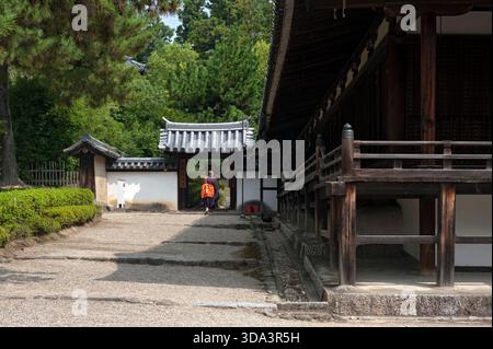 Sacerdote buddista giapponese che cammina attraverso un cancello accanto a un edificio del tempio del tesoro nazionale presso il tempio Horyuji (法隆寺) a Ikaruga, Nara, Giappone. Foto Stock