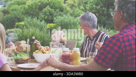 Condivisione del pasto famiglia seduto a un tavolo di legno nel cortile posteriore, uomo con una camicia a quadri rossa che si avvicina alla caraffa Foto Stock