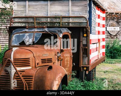 Un camion Dodge d'epoca arrugginito si trova accanto a un edificio agricolo presso le Treiber Farms di Long Island, New York. Vernice sbiadita, legno intemprato e rurale americano Foto Stock