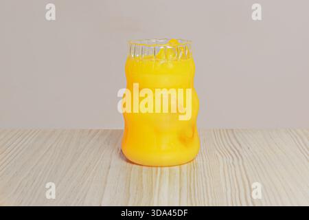 Un bicchiere ricurvo riempito di ghiaccio e succo d'arancia su un tavolo di pino Foto Stock