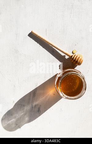 Primo piano di un vaso di vetro riempito di miele dorato e di un cucchiaio di miele di legno Foto Stock