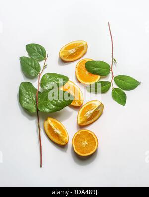 Fette e metà arancioni su sfondo bianco con rami di foglie verdi. Rinfrescante concetto estivo con agrumi e foglie verdi. Vista dall'alto. Foto Stock