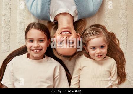 Una madre e le figlie sorridenti si godranno un momento di gioia su un tappeto bianco, mostrando legame familiare e felicità in un ambiente accogliente pieno di calore a Foto Stock