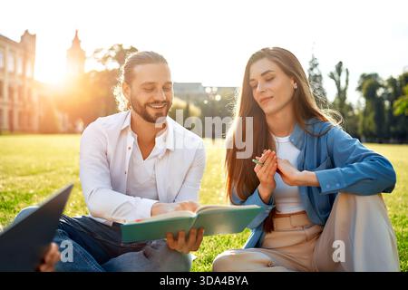Una giovane coppia si diverte a trascorrere un soggiorno piacevole e tranquillo nel parco, studiando e scambiando idee dai libri in una giornata di sole. Si legano attraverso l'accademico di Foto Stock