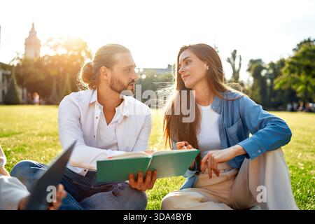 Una giovane coppia si diverte a trascorrere un soggiorno piacevole e tranquillo nel parco, studiando e scambiando idee dai libri in una giornata di sole. Si legano attraverso l'accademico di Foto Stock